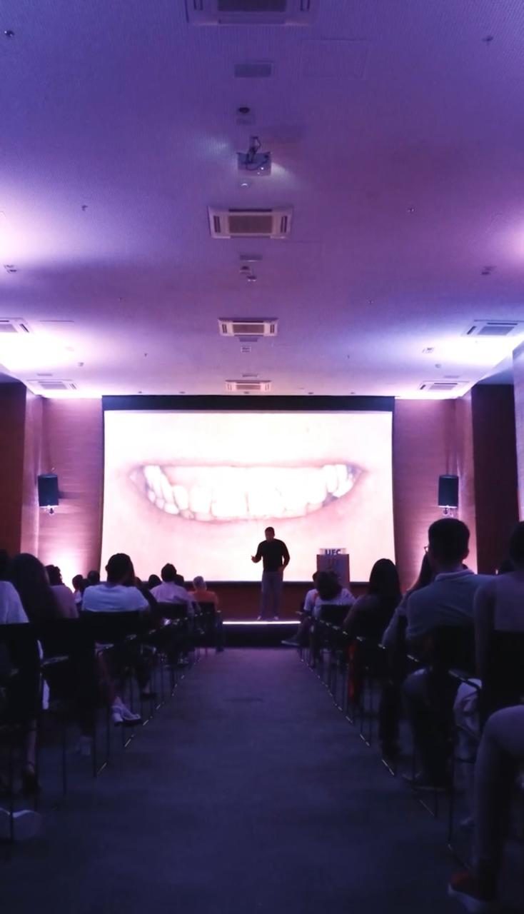 Telão exibindo caso clínico de laminados cerâmicos para plateia de dentistas em auditório