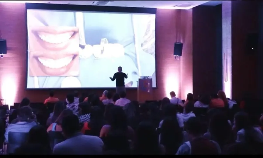 Plateia acompanha comparação de antes e depois de laminados cerâmicos em telão durante palestra