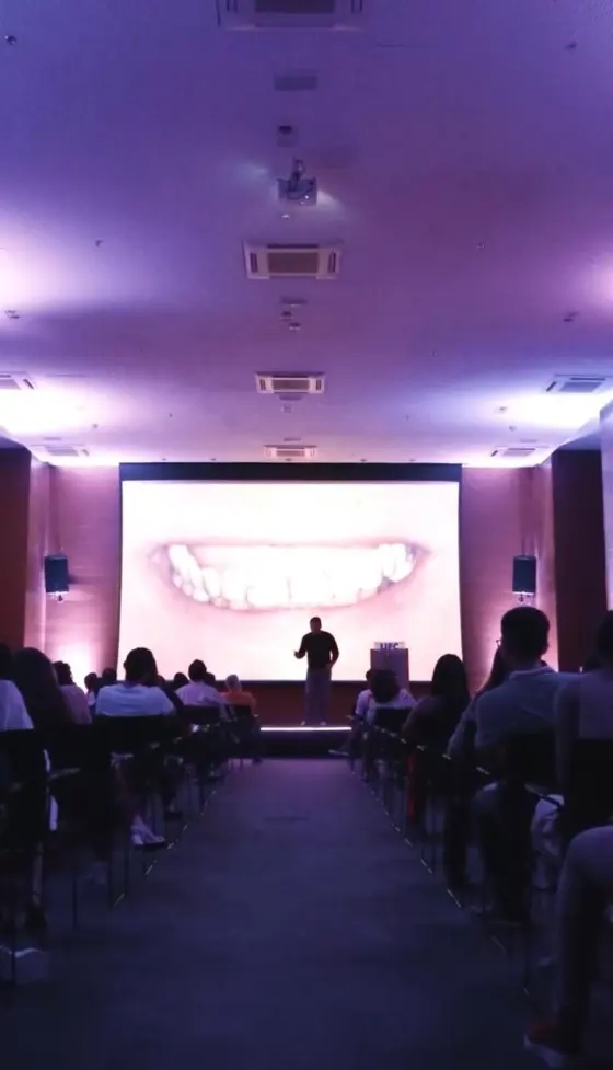 Telão exibindo caso clínico de laminados cerâmicos para plateia de dentistas em auditório