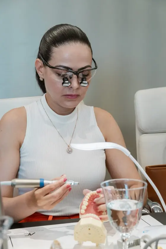 Aluna com loupes praticando ajuste de laminados cerâmicos em modelo